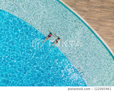 Two kids relax at the edge of clear blue pool during sunny summer vacation. This aerial view captures family, friends, fun, and recreation at resort, relaxation and joyful outdoor moments. Two kids relax at the edge of clear blue pool during sunny summer vacation. This aerial view captures family, friends, fun, and recreation at resort, relaxation and joyful outdoor moments. 122085461