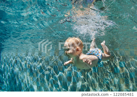 Funny photo of active baby swimming and diving in pool with fun - jump deep down underwater . Family lifestyle and summer children water sports activity and lessons with parents. 122085481