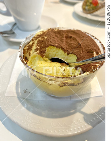 Tiramisu sprinkled with cocoa on saucer with teaspoon. Food and drinks. Traditional Italian dessert. Cappuccino. 122086758
