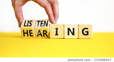Listening or hearing symbol. Businessman turns wooden cubes and changes a concept word Listening to Hearing. Beautiful white background. Copy space. Business educational listening or hearing concept. Listening or hearing symbol. Businessman turns wooden cubes and changes a concept word Listening to Hearing. Beautiful white background. Copy space. Business educational listening or hearing concept. 122086847
