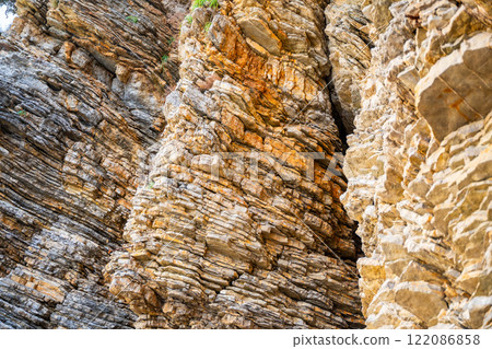 Layered rock texture in Budva, Montenegro. Sedimentary rocks with rugged surface of gray and brown. Natural formation of layers and cracks, geological structure. 122086858