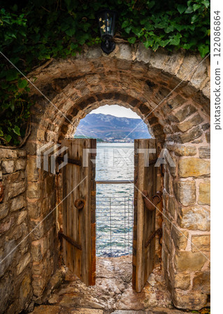 Old street in old town of Budva without people in winter time with small gate in the end to sea coast, Montenegro.  122086864