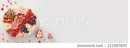 Charcuterie Valentines Day board with chocolate sweets, red hearts, strawberries, blueberries and candies on white background. View from above. Happy Galentines Day. Banner. 122087685