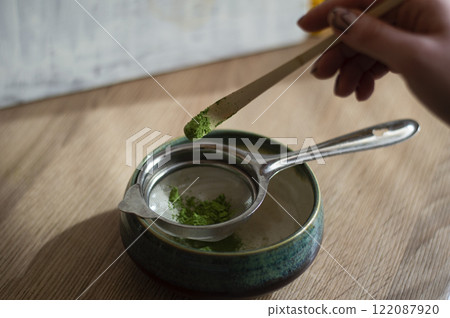 Process of preparing matcha green tea in a bowl on a wooden table. Matcha on a Chasaku spoon Process of preparing matcha green tea in a bowl on a wooden table. Matcha on a Chasaku spoon 122087920