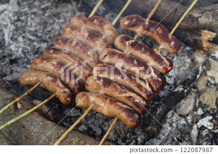 Grilled sausages on the coals of a campfire Grilled sausages on the coals of a campfire 122087987