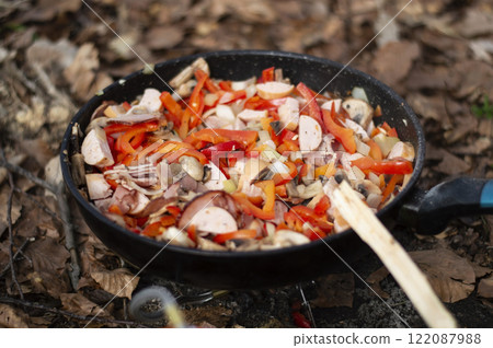 Cooking sausages with vegetables in a frying pan in the forest Cooking sausages with vegetables in a frying pan in the forest 122087988