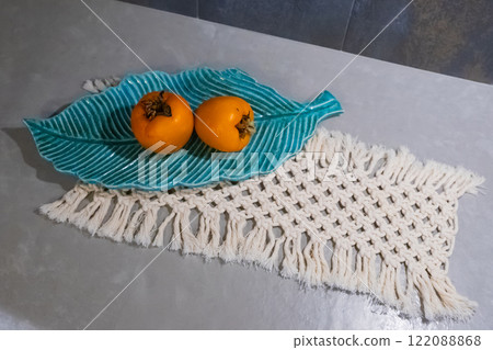 persimmons displayed in bowl on a macrame decor woven textile in table of kitchen 122088868