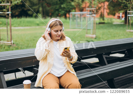 Closeup portrait of a lovely young female listening to music through wireless earphones on nature background. Music lover enjoying music. Woman record voice by mobile cell phone Dictaphone 122089655