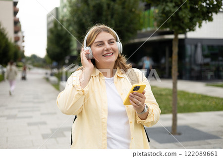 Closeup portrait of a lovely young female listening to music through wireless earphones on urban background. Music lover enjoying music. Woman record voice by mobile cell phone Dictaphone 122089661