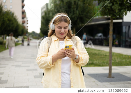 Closeup portrait of a lovely young female listening to music through wireless earphones on urban background. Music lover enjoying music. Woman record voice by mobile cell phone Dictaphone 122089662