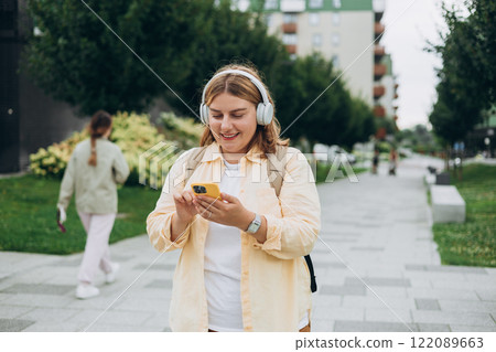 Closeup portrait of a lovely young female listening to music through wireless earphones on urban background. Music lover enjoying music. Woman record voice by mobile cell phone Dictaphone 122089663