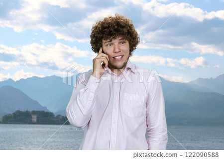 Happy smiling caucasian man in white shirt talking on the phone on vacation. Blue nature landscape in the background. Sea and mountains. Happy smiling caucasian man in white shirt talking on the phone on vacation. Blue nature landscape in the background. Sea and mountains. 122090588