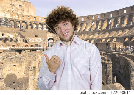 Portrait of happy cheerful young man with curly hair pointing back with his thumb. Ancient coliseum in the background. Portrait of happy cheerful young man with curly hair pointing back with his thumb. Ancient coliseum in the background. 122090615
