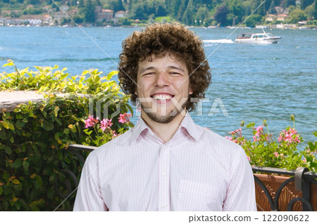 Portrait of a cheerful happy man with curly hair on vacation. Summer lake in the background. Portrait of a cheerful happy man with curly hair on vacation. Summer lake in the background. 122090622