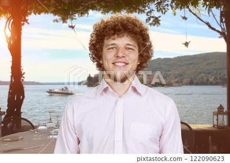Portrait of a handsome smiling man with curly hair on vacation. Evening seascape in the background. 122090623