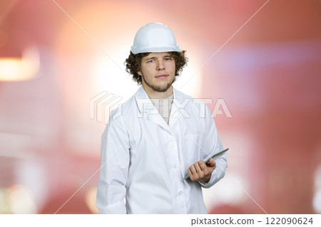 Portrait of a young guy in white uniform holding tablet pc device. Glowing light in the background. Portrait of a young guy in white uniform holding tablet pc device. Glowing light in the background. 122090624