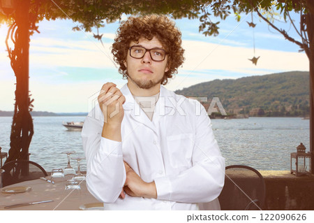 Portrait of a smart thoughtful young man with curly hair wearing glasses. Evening summer landscape in the background. Portrait of a smart thoughtful young man with curly hair wearing glasses. Evening summer landscape in the background. 122090626