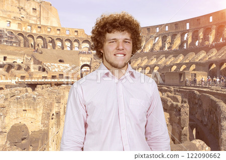 Happy young attractive man with curly hair bites his lip. Ancient coliseum in the background. Happy young attractive man with curly hair bites his lip. Ancient coliseum in the background. 122090662