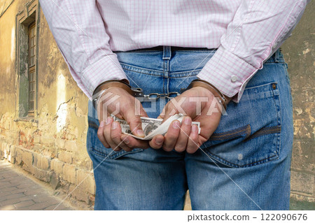 Close up mans hands in handcuffs holding dollar banknotes. Shabby building wall in the background. 122090676