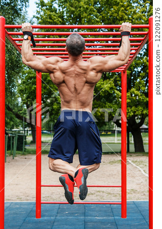 Muscular man doing pull-ups on horizontal bar 122091276