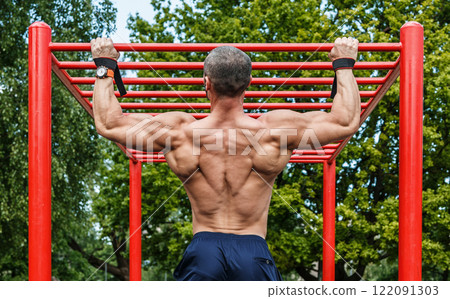 Muscular man doing pull-ups on horizontal bar Muscular man doing pull-ups on horizontal bar 122091303