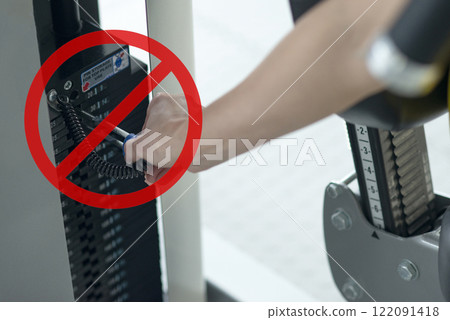 Adjusting gym equipment weight with red prohibition sign symbolizing safety precautions or improper usage warning Adjusting gym equipment weight with red prohibition sign symbolizing safety precautions or improper usage warning 122091418
