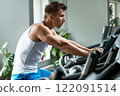 Young muscular man on exercise bike in gym 122091514