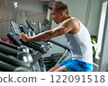 Young muscular man on exercise bike in gym 122091518