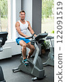 Young muscular man on exercise bike in gym 122091519