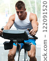 Young muscular man on exercise bike in gym 122091520