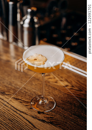 Exquisite yellow cocktail garnished with dried apple on bar counter, perfect for mixology themes Exquisite yellow cocktail garnished with dried apple on bar counter, perfect for mixology themes 122091701