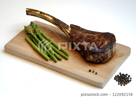 Grilled tomahawk steak with asparagus and peppercorns on cutting board 122092156