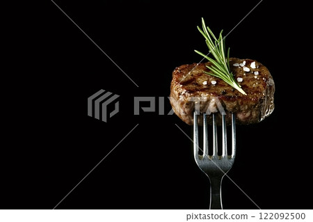 Grilled meat with rosemary and salt on a fork on black background 122092500