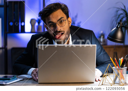 Office businessman hiding behind laptop computer making funny silly face fooling around, disrespect Office businessman hiding behind laptop computer making funny silly face fooling around, disrespect 122093056