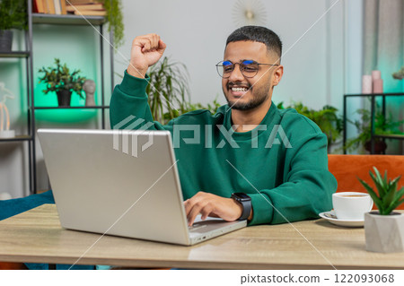 Amazed Indian man use laptop computer, receive good news message shocked by victory, celebrate win 122093068