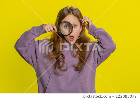 Child girl kid holds magnifying glass near face looking at camera with big zoomed eye, analyzing 122093072