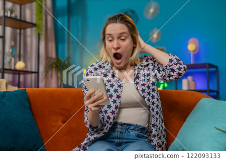 Surprised excited young woman winner holding smartphone reading good news amazed by online game win 122093133