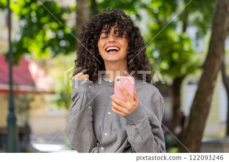 Caucasian woman use mobile smartphone celebrating win good message news outdoors on city street Caucasian woman use mobile smartphone celebrating win good message news outdoors on city street 122093246