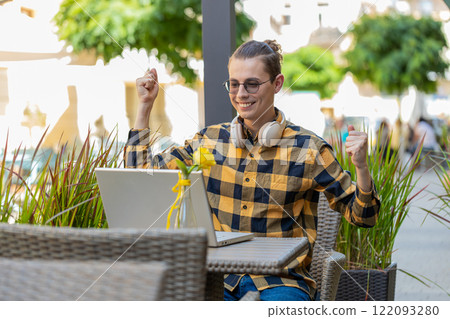 happy man tourist using laptop computer celebrating win good message news in urban city cafe terrace 122093280