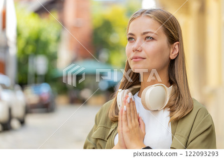Young Caucasian woman meditating, breathes deeply with hands clasped, praying eyes closed on street 122093293