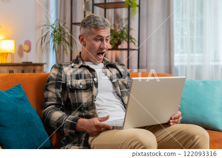 Amazed young man use laptop computer, receive good news message, shocked by victory, celebrate win 122093316