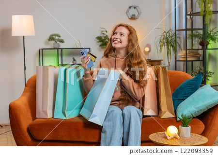 Excited young Caucasian woman with shopping bags receiving order sitting on sofa couch at home 122093359