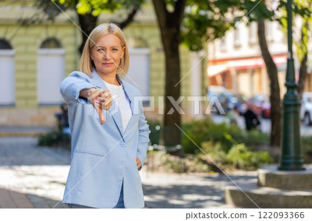 Upset mature Caucasian blonde businesswoman in formal suit looking camera and showing thumb down Upset mature Caucasian blonde businesswoman in formal suit looking camera and showing thumb down 122093366