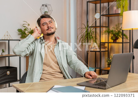 Happy relaxed overjoyed young Caucasian man in wireless headphones listening to music in home room 122093371