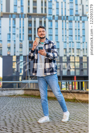 Happy man using smartphone while enjoying morning to-go coffee hot drink against modern building 122093379