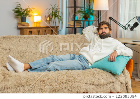 Tired Indian handsome young man guy enjoy relaxing lying on sofa in living room at home apartment 122093384