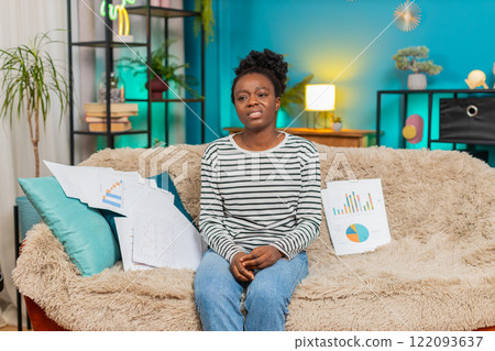 African American woman upset stressed with financial problems sitting at home, looking at documents 122093637
