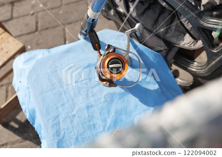 A fishing reel displayed on blue cloth in a picturesque outdoor setting A fishing reel displayed on blue cloth in a picturesque outdoor setting 122094002