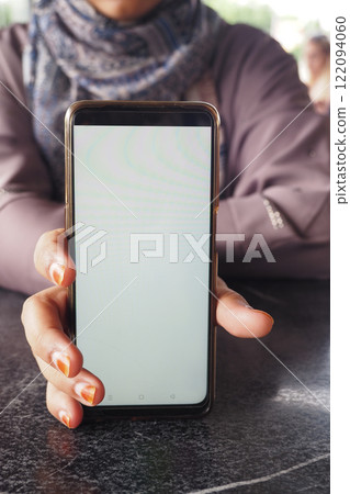 A person is holding a smartphone with a blank screen while sitting at a table A person is holding a smartphone with a blank screen while sitting at a table 122094060