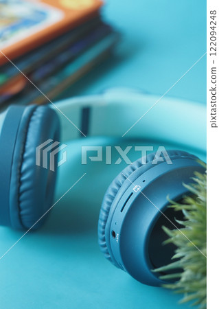 Stylish Blue Headphones with Books and Green Plant on Teal Surface Stylish Blue Headphones with Books and Green Plant on Teal Surface 122094248